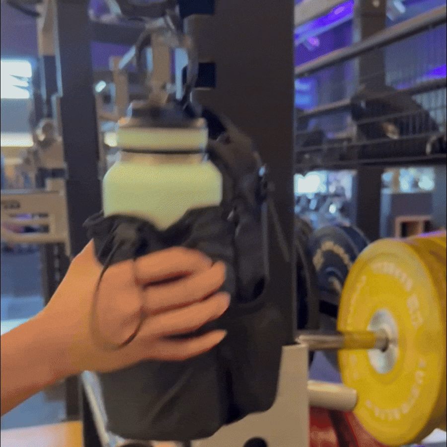 A person holding a water bottle attached to the Titan Gym Bag by HolyH₂O™, showcasing its magnetic gym bag feature.
